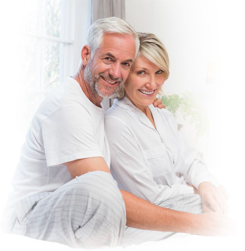 happy older couple sitting on bed in white room